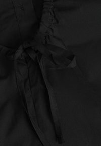 Tessuto nero con cintura arricciata e cordino regolabile. Il materiale è liscio con una finitura opaca, senza motivi visibili o elementi metallici.