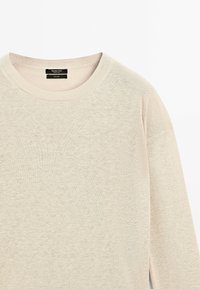 Maglione lavorato a maglia in beige chiaro con scollatura rotonda, vestibilità ampia e tessuto testurizzato. Etichetta visibile all'altezza della scollatura.