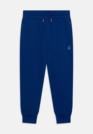 Pantalon de jogging bleu marine avec taille élastique, cordon, poches latérales, chevilles côtelées et petite broderie blanche d'un smiley sur la cuisse gauche.