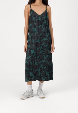 Green floral maxi dress with black leaf pattern, spaghetti straps, pleated design, paired with gray sneakers and white socks. Smooth texture.