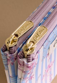 Lillemustriline riidest rahakott siniste ja valgete triipudega. Varustatud kahe kuldse metallist tõmblukuga, millel on tekstuuriga tõmburid ja riidest ääris.