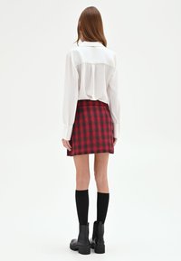 Blusa bianca a maniche lunghe abbinata a una minigonna a quadri rossa e nera, calzini neri al ginocchio e stivali neri robusti. Semplici dettagli con bottoni.