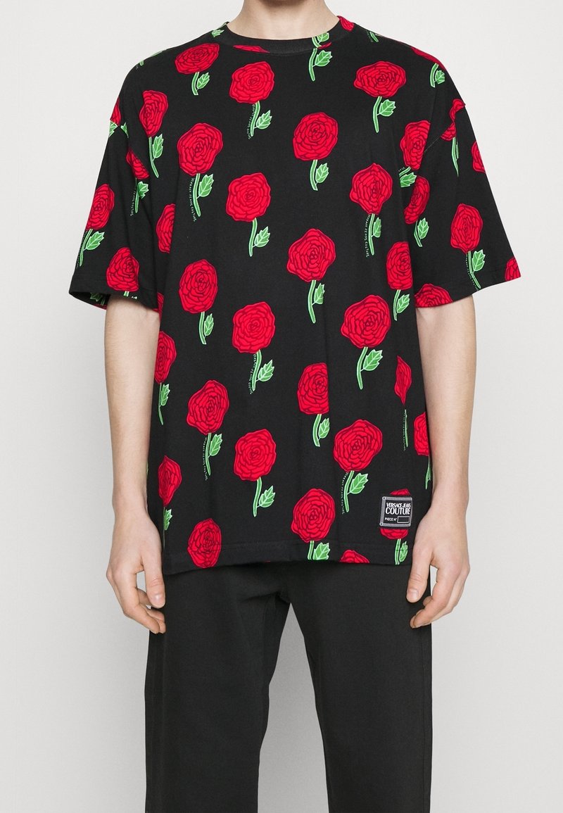 Svart t-shirt med ett upprepat mönster av röda rosor med gröna blad. Tillverkad av bomull med korta ärmar och en etikett vid fållen.