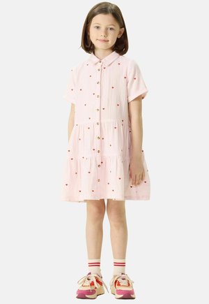 Rosa Kurzarmkleid mit roten Herzmustern, Knopfleiste und gestuftem Design, kombiniert mit bunten Sneakern und gestreiften Socken.