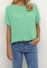 Mintgrøn kortærmet top med løs pasform og let tekstureret stof, parret med lyseblå high-waisted jeans.