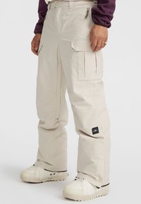 Beige cargo pants with multiple pockets, a straight-leg design, and reinforced seams. Features a brand patch on the left leg.