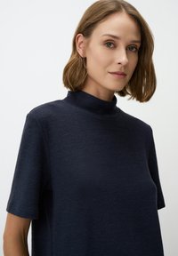 Top blu navy a collo alto in tessuto morbido e texturizzato con maniche corte, caratterizzato da una vestibilità rilassata e un design minimalista.