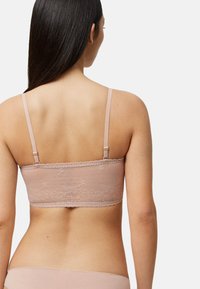 Bralette de encaje color nude con tirantes ajustables, patrones florales y de puntos, tela texturizada y borde festoneado a lo largo de la banda.
