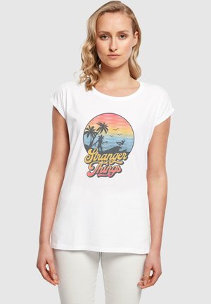 Hvit bomull T-skjorte med et fargerikt sirkulært grafikk med palmer, solnedgangstriper og teksten "Stranger Things" i en retro skrift.