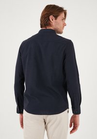 Camisa de manga larga azul marino con un acabado texturizado, puños abotonados y cuello clásico. Corte ajustado y diseño de dobladillo curvado.