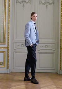 Gaiši pelēks bleizeris, balts krekls, melna tauriņsaites, melnas bikses un brūni ādas apavi. Gluda auduma, pielāgota piegriezuma un formāls dizains.