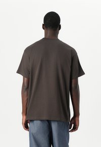 T-shirt en coton marron à manches courtes et col rond standard, offrant une coupe décontractée et une texture lisse. Aucun motif ou accent visible.