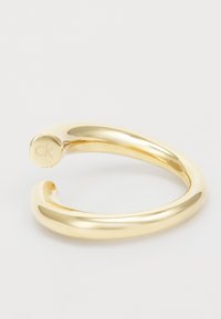 Pulsera de muñeca de color dorado con un acabado elegante y suave y un sutil grabado "ck". Diseño abierto con bordes redondeados.