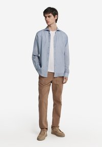 Ljusblå randig skjorta i lätt material, matchad med beige byxor och beige skor. Skjortan har en knäppning framtill och krage.