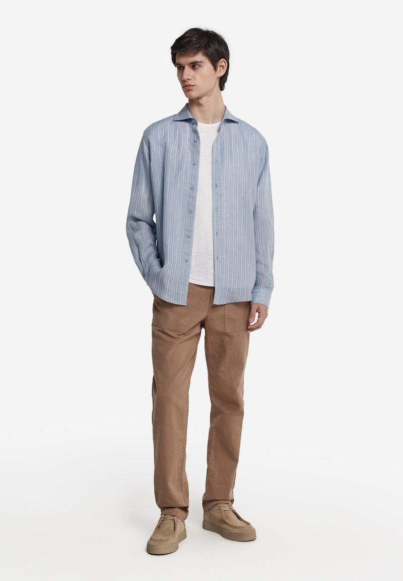 Ljusblå randig skjorta i lätt material, matchad med beige byxor och beige skor. Skjortan har en knäppning framtill och krage.