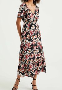 Blommig maxiklänning med svart bakgrund och röda samt vita blommor, korta ärmar, V-ringning och flerradig nederdel. Remsandaler i svart.