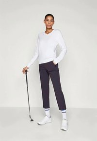 Suéter branco com decote em V, calças náuticas até os tornozelos, ténis brancos, segurando um taco de golfe. Design simples; textura suave; corte atlético.