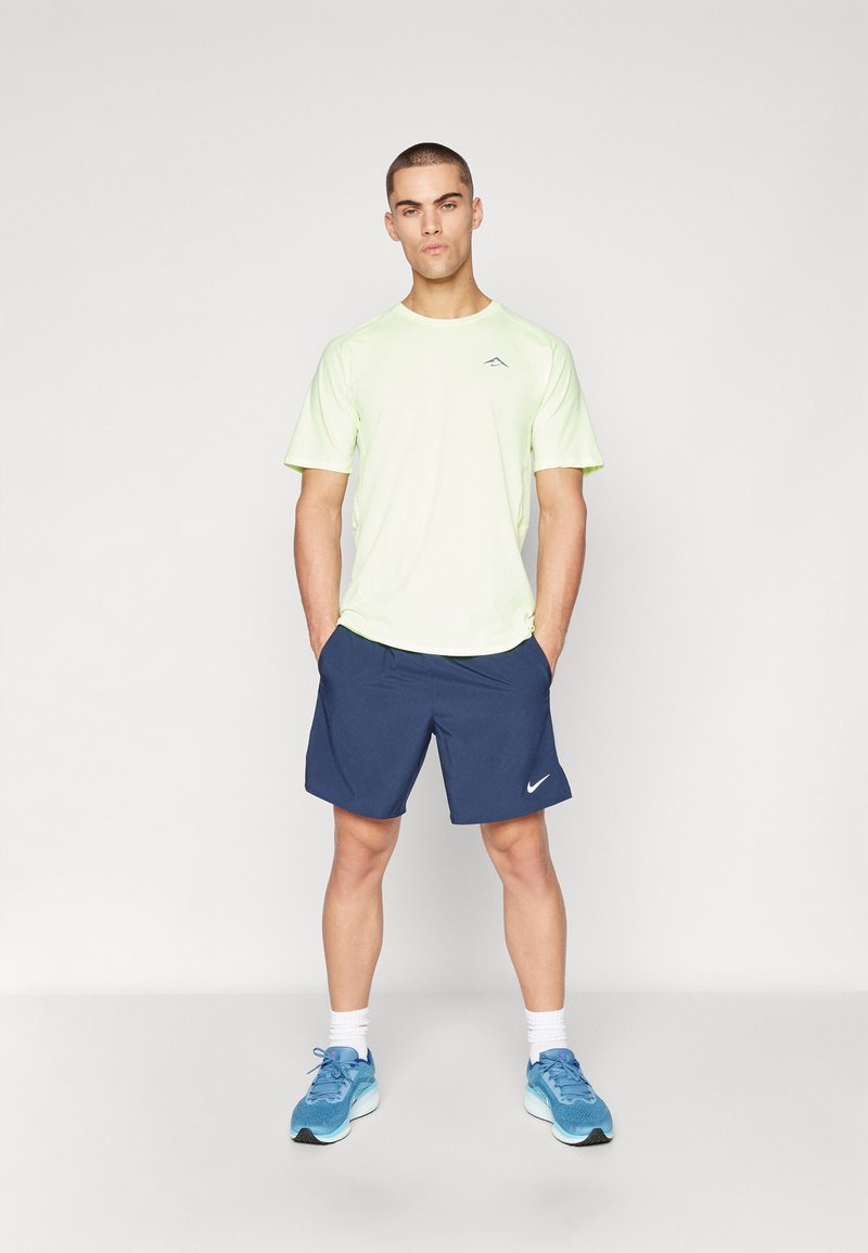 T-shirt de sport jaune clair à manches courtes et short bleu marine. Comprend un logo bleu sur le t-shirt et un emblème blanc Nike sur le short.
