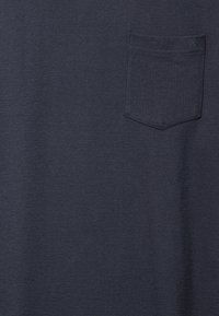 Sötétszürke kötött anyag kis mellzsebbel, mely finom varrással és dekoratív X részlettel rendelkezik a felső sarokban.