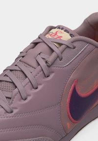 Baskets violettes avec un swoosh Nike rose et violet foncé, une langue texturée et des lacets violets assortis noués à l'avant.