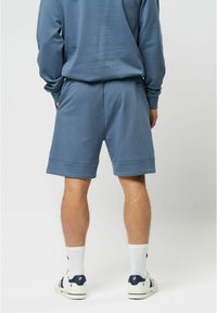 Blauwe sportshorts met een relaxte pasvorm, zijzakken en een gladde textuur, gecombineerd met witte crew-sokken en kleurrijke casual schoenen.