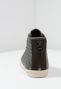 Šedá prošívaná kotníková bota s kontrastním tmavě hnědým textilním panelem a zadním zipem. Krémová podešev a zaoblený tvar špičky.