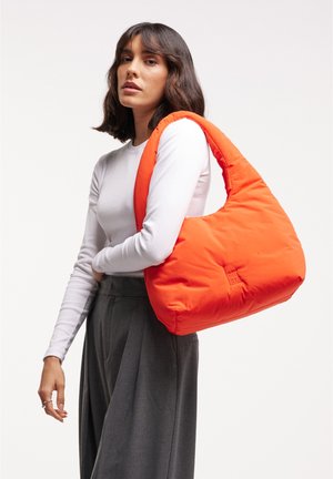 Borsa a spalla arancione, morbida e con una forma rilassata, caratterizzata da una texture liscia, un dettaglio del logo sul davanti e una tracolla larga per il trasporto.