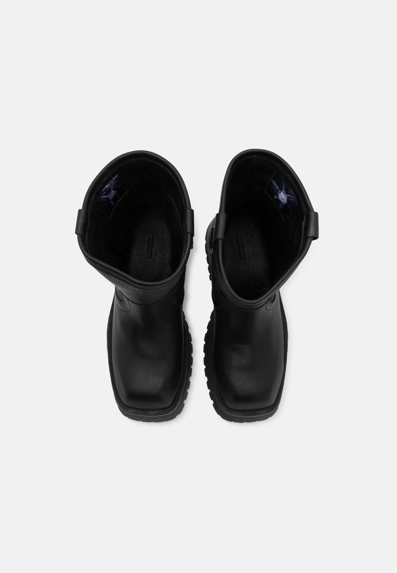 Stivali neri impermeabili con punta arrotondata, suole texture e manici ad anello nella parte superiore per facilitarne l'indossamento. Esterno in pelle liscia.