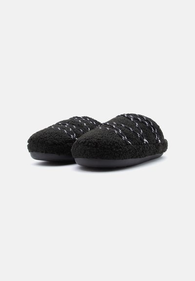 Chaussons en polaire noire avec une surface texturée, présentant des motifs croisillons blancs et une semelle en caoutchouc noire. Conception à bout arrondi.