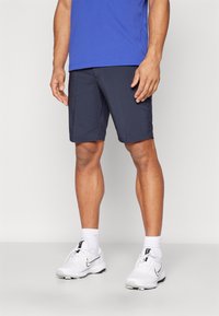 Marineblå idrettsshorts med rett snitt, kombinert med hvite joggesko som har svarte detaljer og teksturerte hvite sokker.