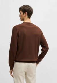 Brun stickad tröja med långa ärmar och rundad halsringning. Mjuk textur, figurnära design, baksidan visar en minimalistisk stil och rena linjer.