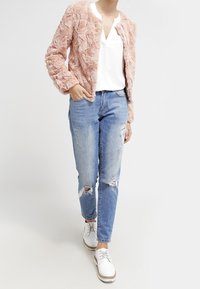 Kurtka z sztucznego futra w delikatnym różowym kolorze, o fakturowanej powierzchni. Noszona na białej bluzce z dekoltem w serek, w połączeniu z przetartymi jasnoniebieskimi dżinsami i białymi butami.