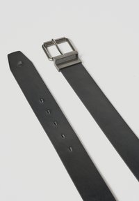 Cinturón de cuero negro con hebilla metálica rectangular plateada y múltiples agujeros de ajuste sobre un fondo claro.