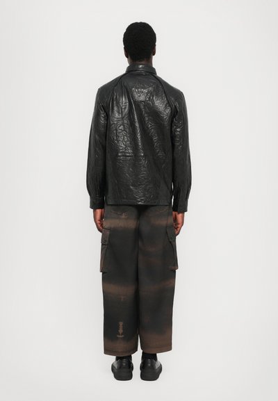 Black crinkled leather jacket with a collar, paired with loose, dark brown cargo pants featuring pockets and distinct faded patterns.