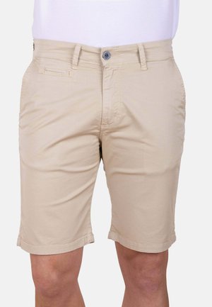 Pantalones cortos beige hasta la rodilla con botón delantero, cremallera, trabillas para cinturón y bolsillos laterales, usados con una camisa blanca.
