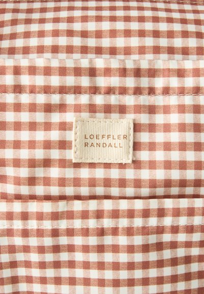Ύφασμα σε μπεζ και λευκό καρό με ραμμένη ορθογώνια ετικέτα που γράφει "LOEFFLER RANDALL" με ανοιχτό καφέ γράμματα.
