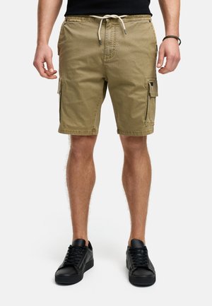 Shorts cargo en khaki, avec une taille à cordon de serrage, des poches latérales et un tissu texturé. Associés à des baskets noires.