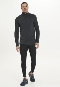 Langærmet, charcoal halv-zip pullover lavet af letvægtsmateriale; tætsiddende sorte leggings og sportsko fuldender outfittet.