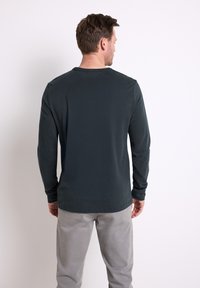 Mörkgrå långärmad skjorta med rund halsringning och en mjuk, len textur, tillsammans med ljusgrå byxor. Inga synliga mönster eller detaljer.