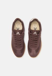 Baskets brunes avec tige en daim et textile, lacets plats, col rembourré et semelle extérieure en caoutchouc. Logo visible sur la languette.