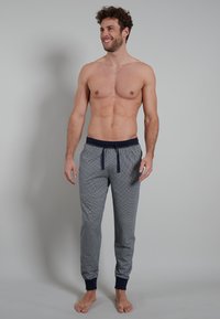 Navy pajama pants with a white dot pattern, elastic waistband and drawstring, cuffed ankles, soft fabric, fitted and tapered design.