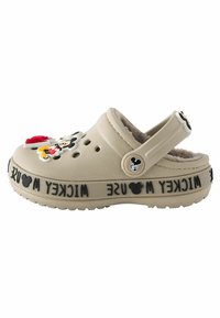 Beige klumpitippa med mjukt inre, prydd med färgglada Mickey Mouse-charms och "Mickey Mouse"-text på bandet; justerbar hälrem.