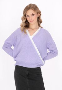 Maglione lavorato a maglia lilla chiaro con un bordo bianco a ondulazione lungo il collo a V, caratterizzato da una vestibilità rilassata e maniche lunghe. Completato da una gonna nera.