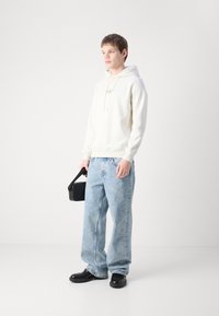 Sudadera blanca con capucha y cordones, vaqueros holgados de color azul claro, zapatos negros y una pequeña bolsa negra de mano. Diseño simple y casual.