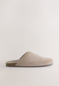Chausson en daim beige à enfiler avec une semelle basse en liège et une bande lisse sur le dessus, présenté de profil sur un fond neutre.