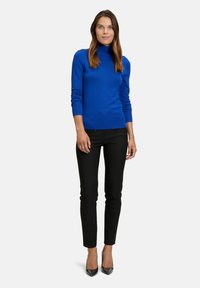 Königsblauer Rollkragenpullover aus weichem Stoff, figurbetontes Design, kombiniert mit schwarzer Slim-Fit-Hose und schwarzen High-Heels.
