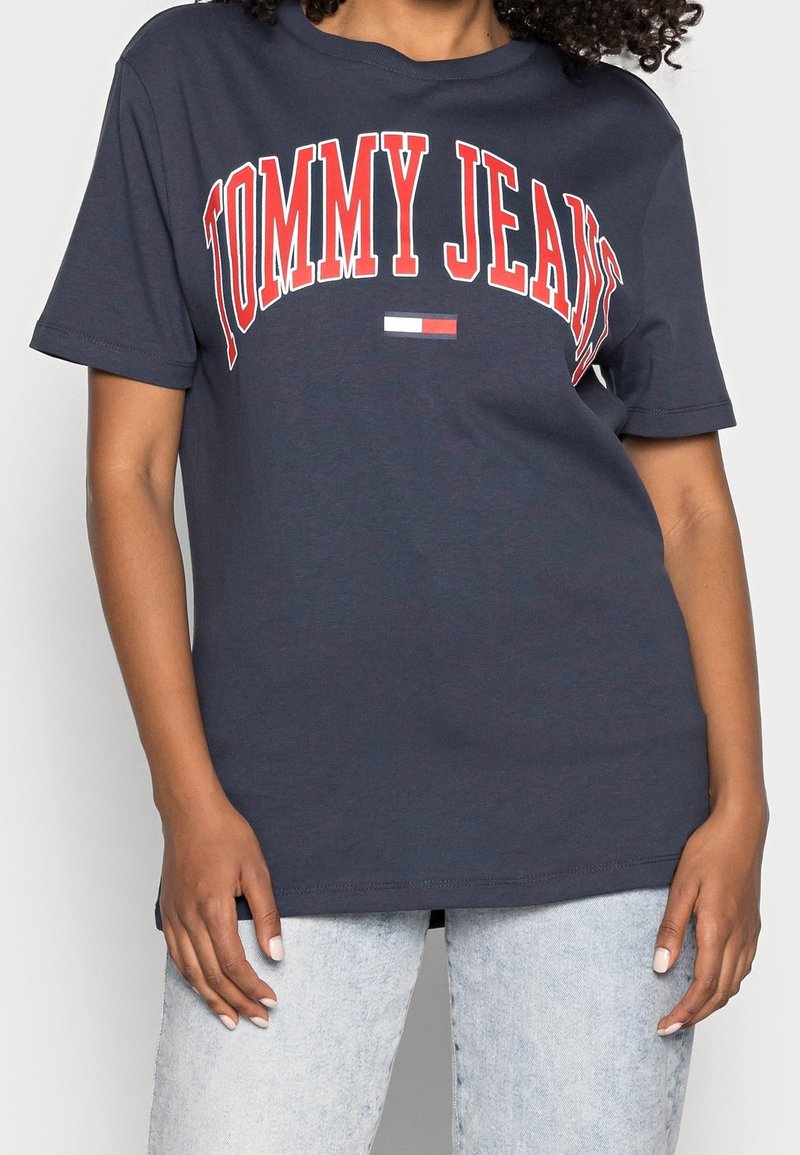 Navy blue cotton t-shirt featuring bold red "TOMMY JEANS" text across the chest and a small logo in red, white, and blue. Short sleeves.