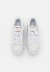 Ett par vita Reebok Classic-sneakers med vita snören, sedd uppifrån på en helt vit bakgrund.