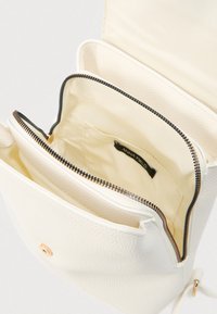 Λευκή υφασμάτινη τσάντα χειρός με φερμουάρ σε θήκη, εσωτερική επένδυση με λεία υφή και διακοσμητικά στοιχεία σε χρυσό τόνο. Λεπτομέρεια κλεισίματος ορατή.