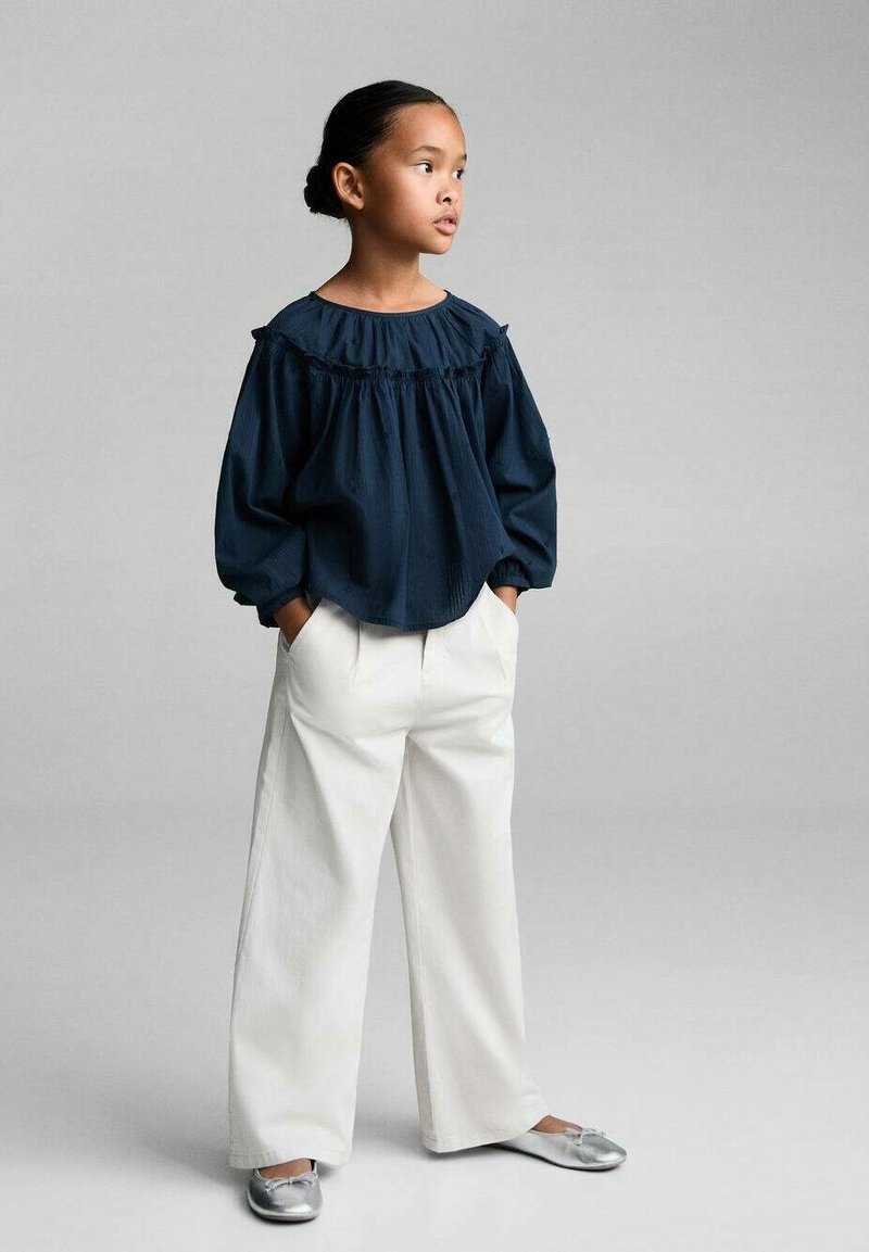 Navyblauw blouse met pofmouwen en ruffles, gecombineerd met witte wijde broek en zilveren platte schoenen. Eenvoudig, schoon ontwerp.
